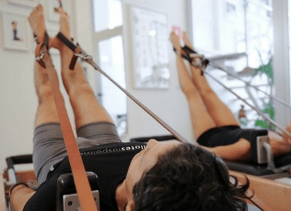 Una mujer está acostada en una máquina de pilates con las piernas levantadas.
