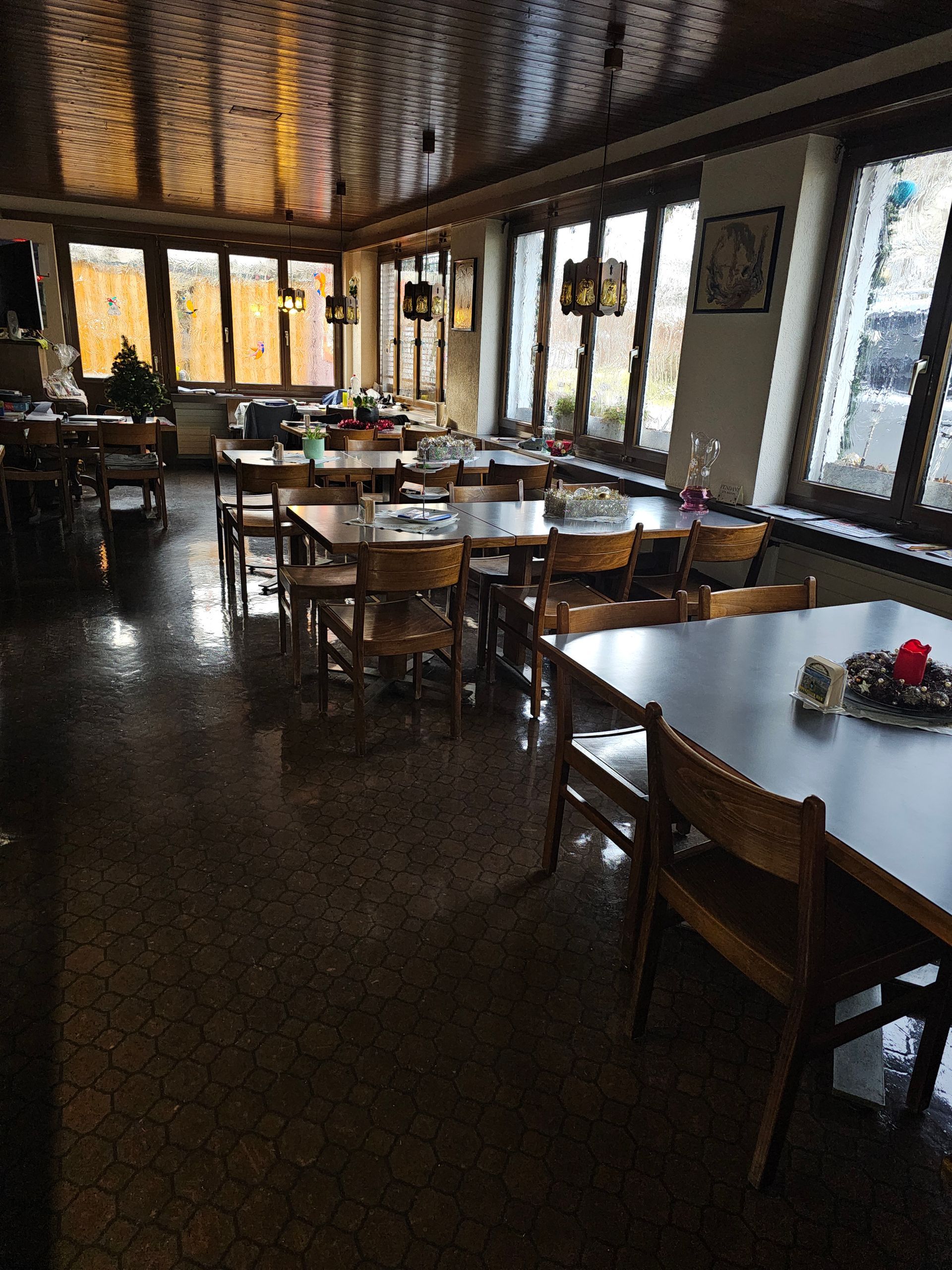 Restaurantinterieur mit Holzwänden, Bar, Tischen, Stühlen und Hängelampen.