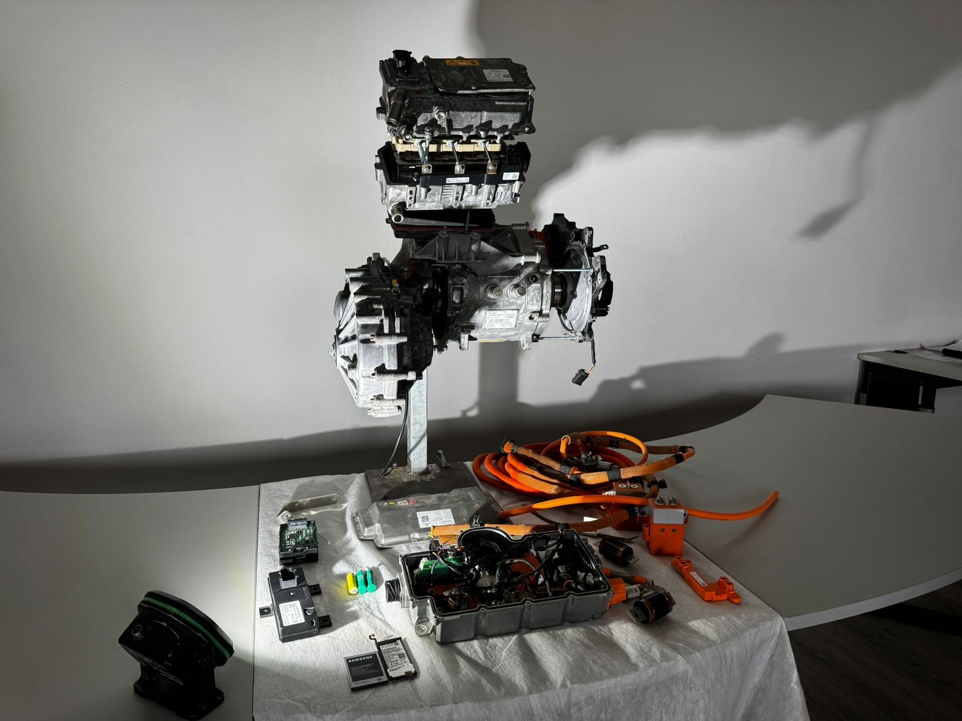 Auf einem Ausstellungstisch steht eine Antriebseinheit für ein Elektrofahrzeug mit zugehörigen elektronischen Bauteilen und orangefarbenen Kabeln.