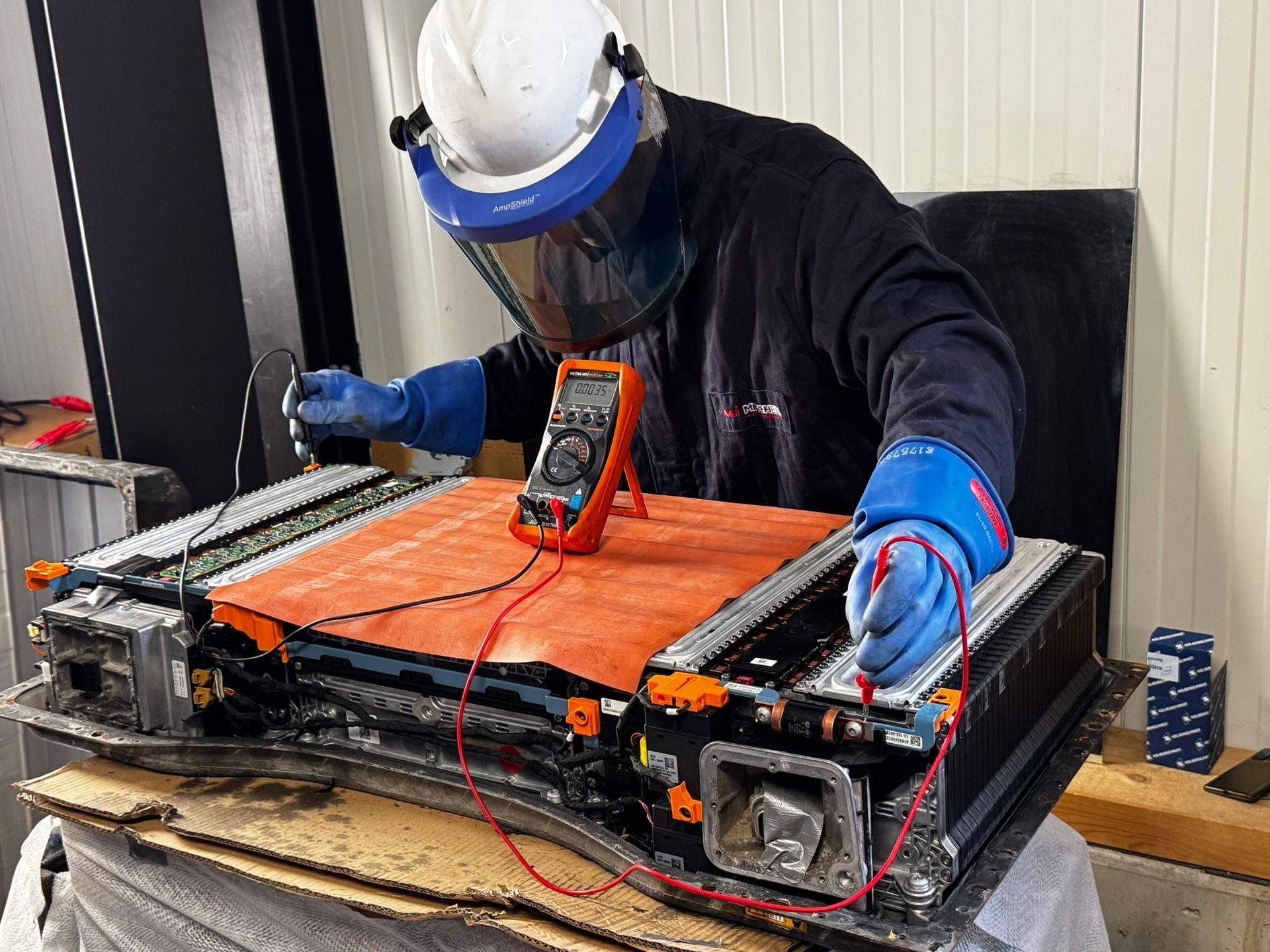 Auf einem Ausstellungstisch steht eine Antriebseinheit für ein Elektrofahrzeug mit zugehörigen elektronischen Bauteilen und orangefarbenen Kabeln.