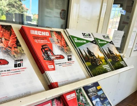 Brochures et magazines présentés sur un présentoir extérieur devant un sol en briques.