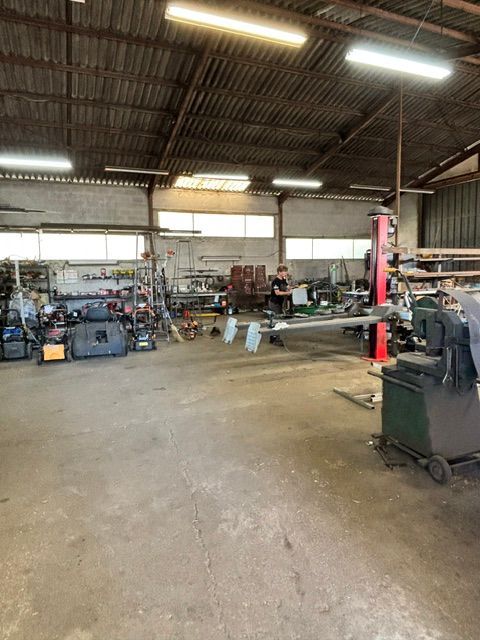 Grand atelier industriel avec outils, équipements et sol en béton éclairé par un éclairage zénithal puissant.