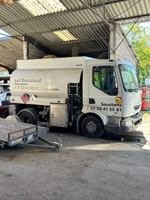Camion-citerne rempli d'engrais stationné sous un hangar, avec une remorque attelée et des arbres visibles à l'extérieur.