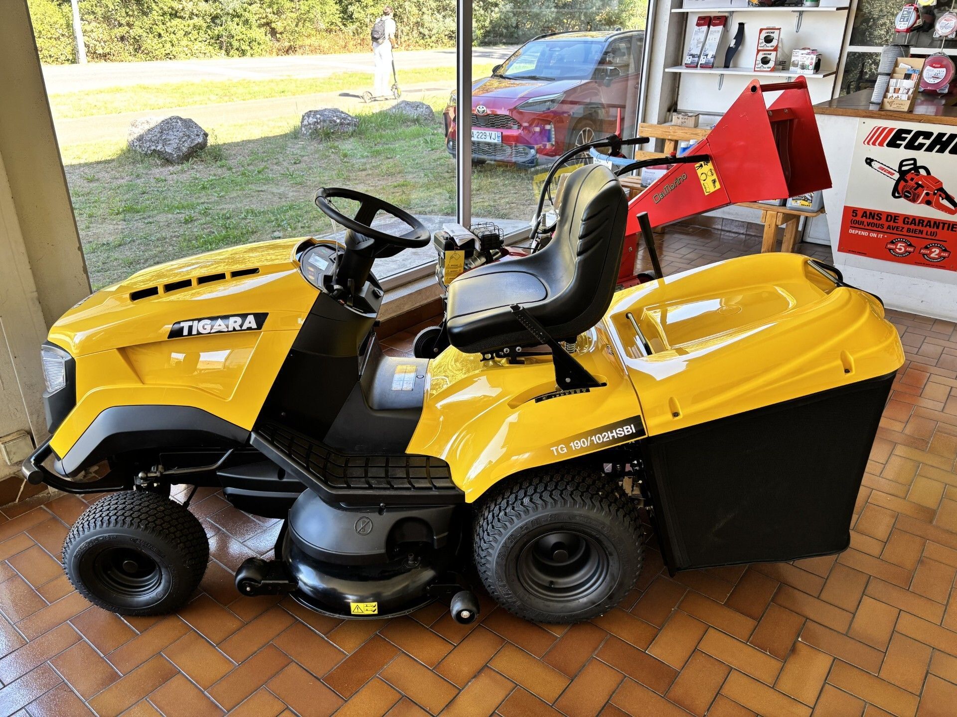 Une tondeuse autoportée se trouve à l'intérieur d'un garage, un camion étant visible à l'extérieur.