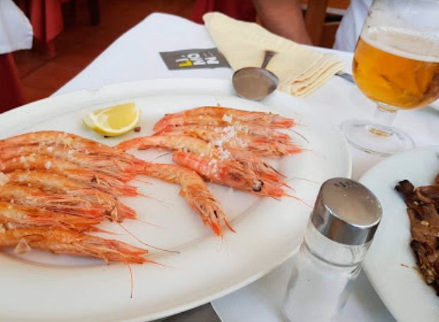 Un plato de camarones se encuentra en una mesa junto a un vaso de cerveza.