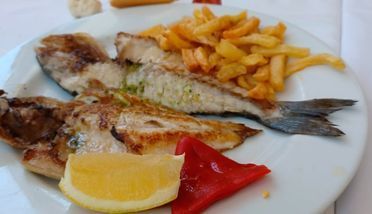 Un plato blanco cubierto con pescado, patatas fritas y pimientos.