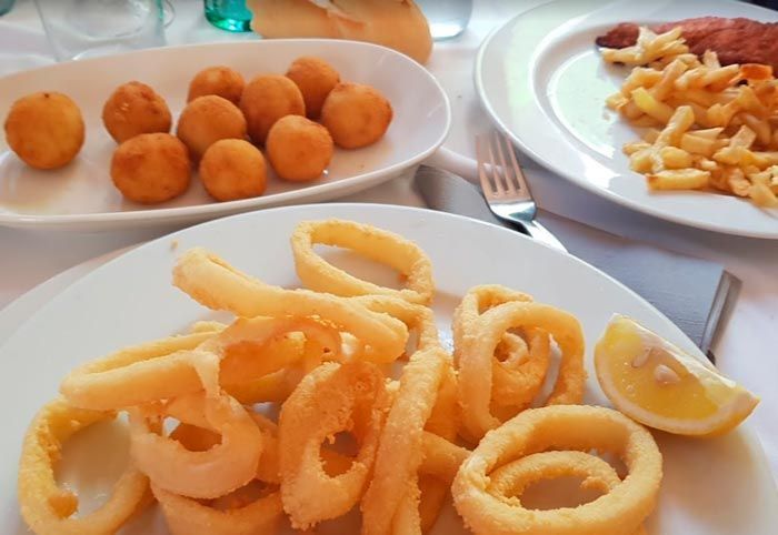 Un plato blanco cubierto con patatas fritas y aros de calamar sobre una mesa.