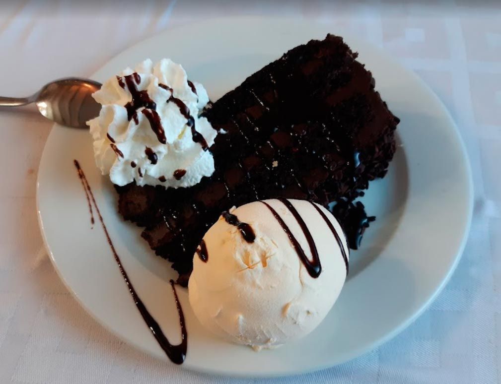 Una rebanada de pastel de chocolate con crema batida y helado en un plato blanco