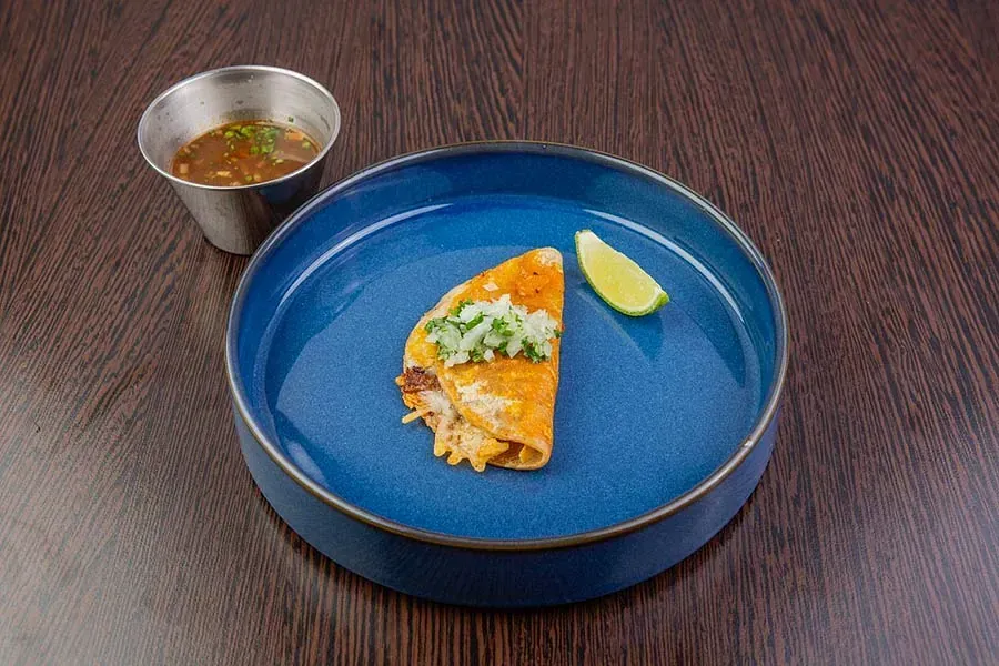 Un plato azul cubierto con un taco y una taza de sopa sobre una mesa de madera.