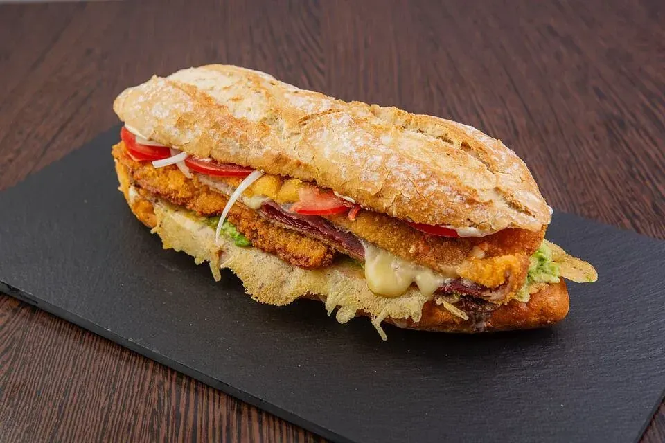 Un sándwich está sobre una tabla de cortar negra sobre una mesa de madera.