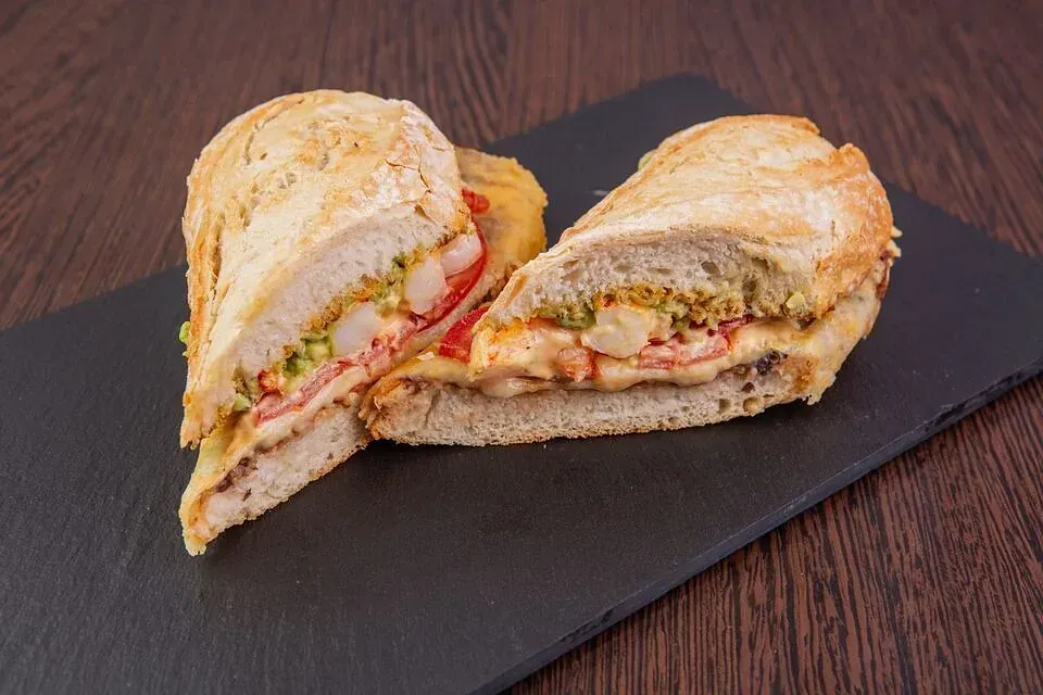 Un sándwich se corta por la mitad en una tabla de cortar negra sobre una mesa de madera.