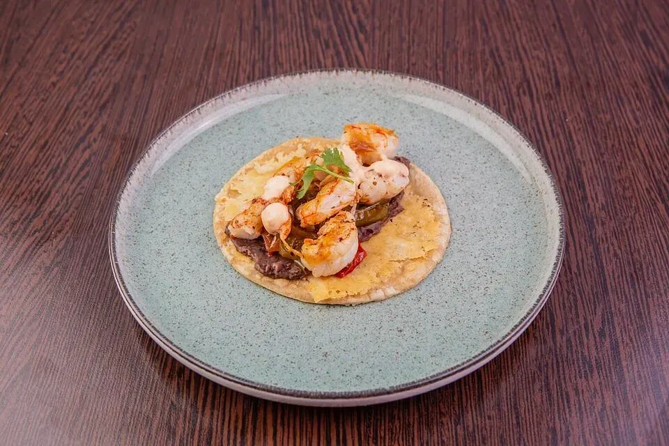 Un taco con camarones y frijoles negros en un plato sobre una mesa de madera.