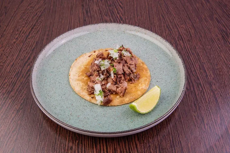 Un taco en un plato con una rodaja de limón sobre una mesa de madera.