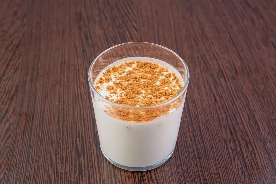 Un vaso de leche con canela encima está sobre una mesa de madera.