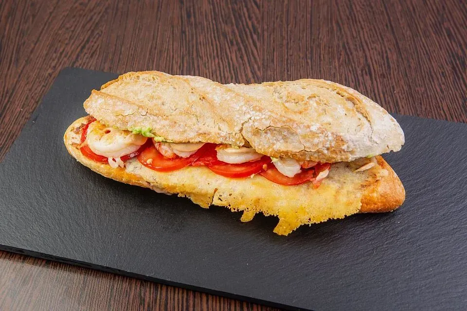 Un sándwich con tomates y queso en un plato negro sobre una mesa.