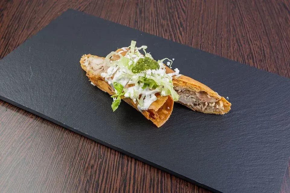 Dos tacos están sentados en un plato negro sobre una mesa de madera.