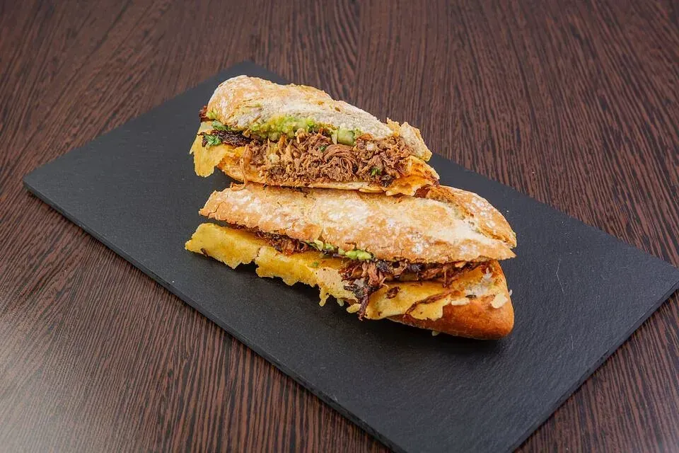 Un sándwich está sobre una tabla de cortar negra sobre una mesa de madera.