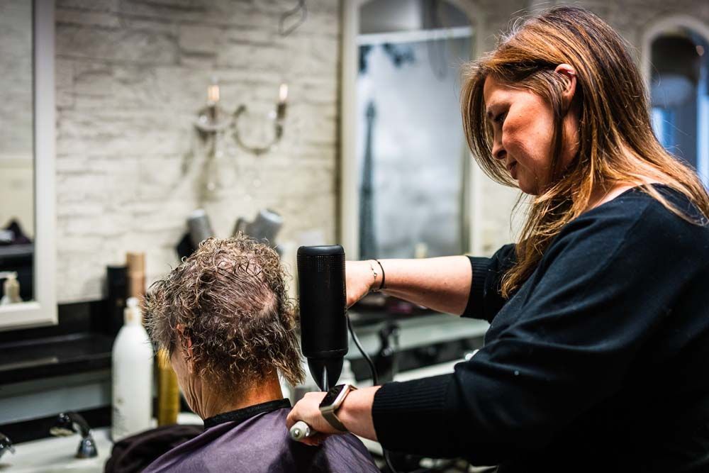 Eine Frau föhnt einem Mann in einem Salon die Haare.