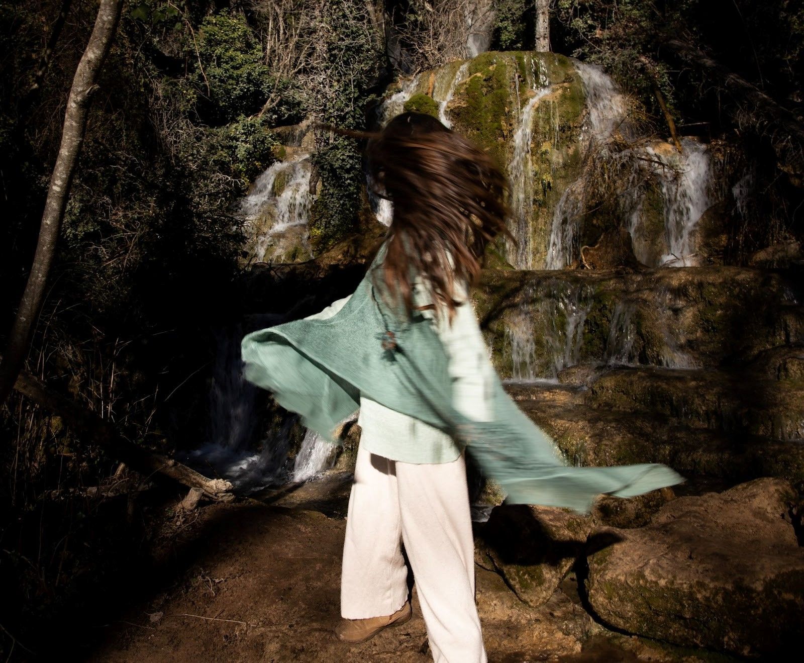 Una mujer con una capa verde está parada frente a una cascada.