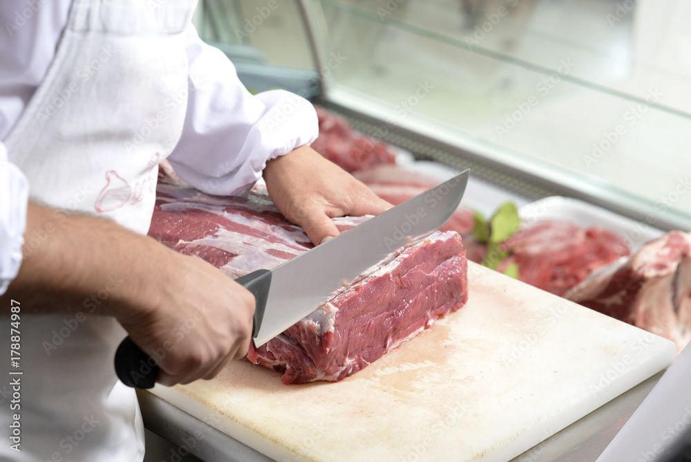 Ein Metzger schneidet rohes Rindfleisch auf einem Schneidebrett in einem Fleischereigeschäft.
