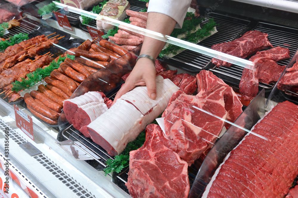 Eine Hand greift in der Fleischtheke nach Rindfleischstücken mit rotem Fleisch und Würsten.