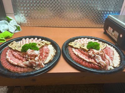 Fleischtheke mit verschiedenen rohen Fleischsorten und Wurstwaren, die unter Glas in einem Markt ausgestellt sind.