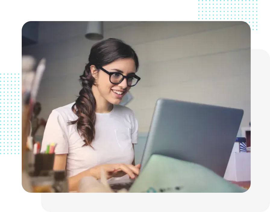 Frau mit Brille lächelt, während sie in einem Büro auf einem Laptop tippt.