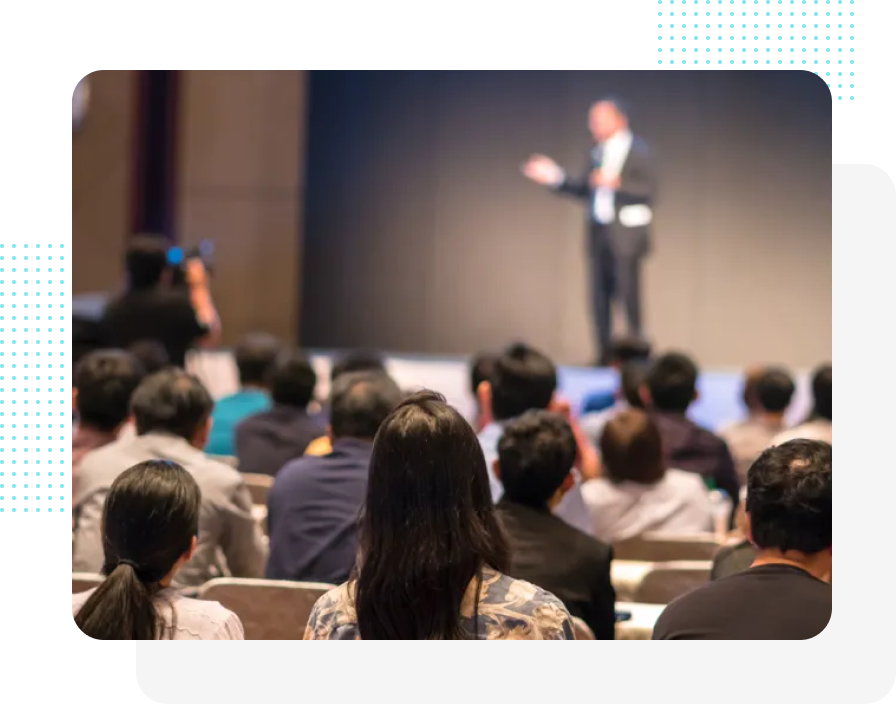 Das Publikum sitzt und beobachtet einen Mann, der auf der Bühne einer Konferenz eine Präsentation hält.