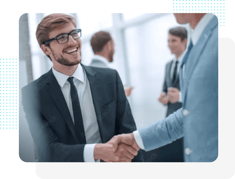 Zwei Geschäftsleute in Anzügen schütteln lächelnd die Hände in einem Büro. Im Hintergrund sind weitere Personen zu sehen.