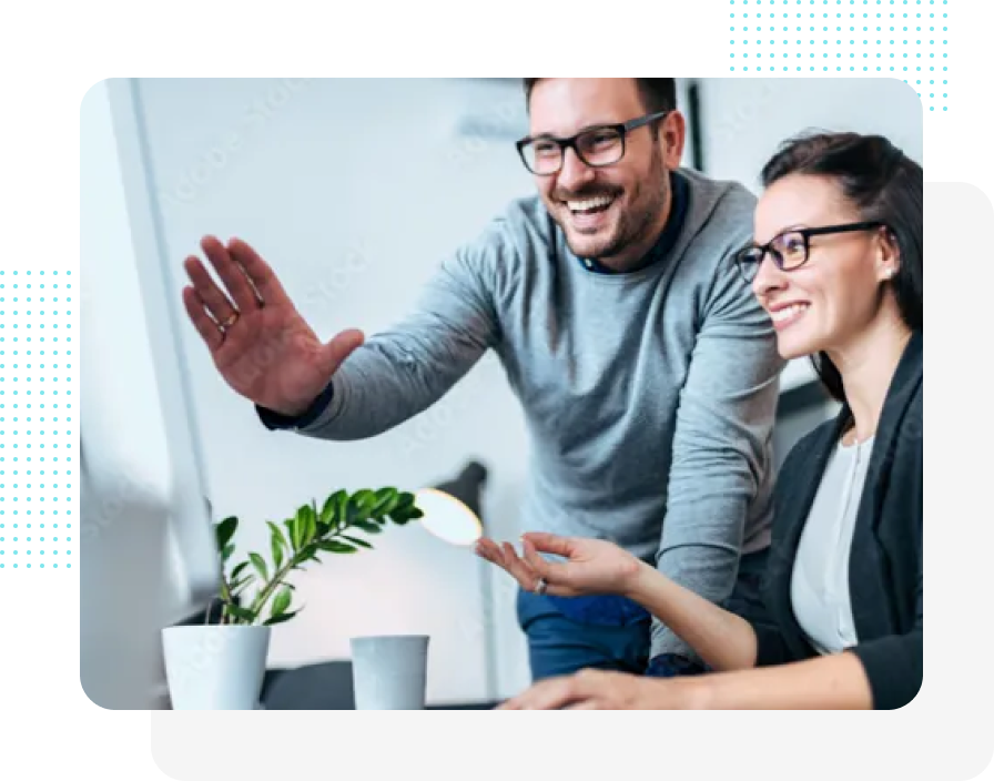 Zwei Kollegen schauen lächelnd auf einen Computer. Mann gestikuliert, Frau zeigt. Büroumgebung.