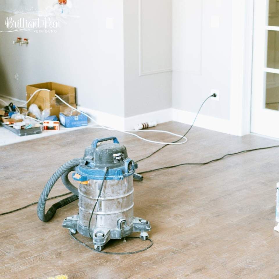 Ein Werkstattsauger auf einem Holzboden in einem im Bau befindlichen Raum, daneben Werkzeuge und eine Steckdose.