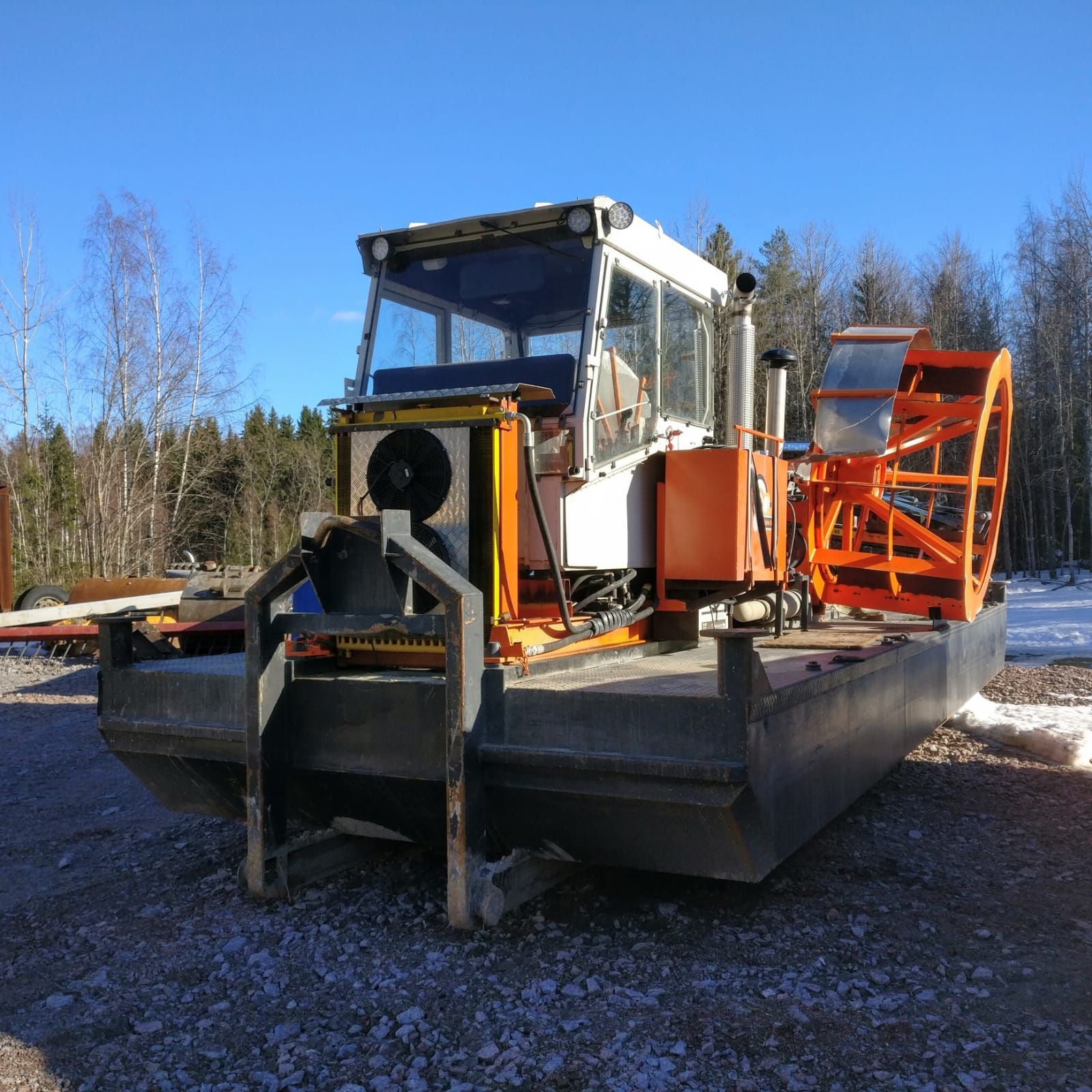 Raskas lumiaura-auto oransseilla aurauslaitteilla pysäköitynä soratontille sinisen taivaan alle