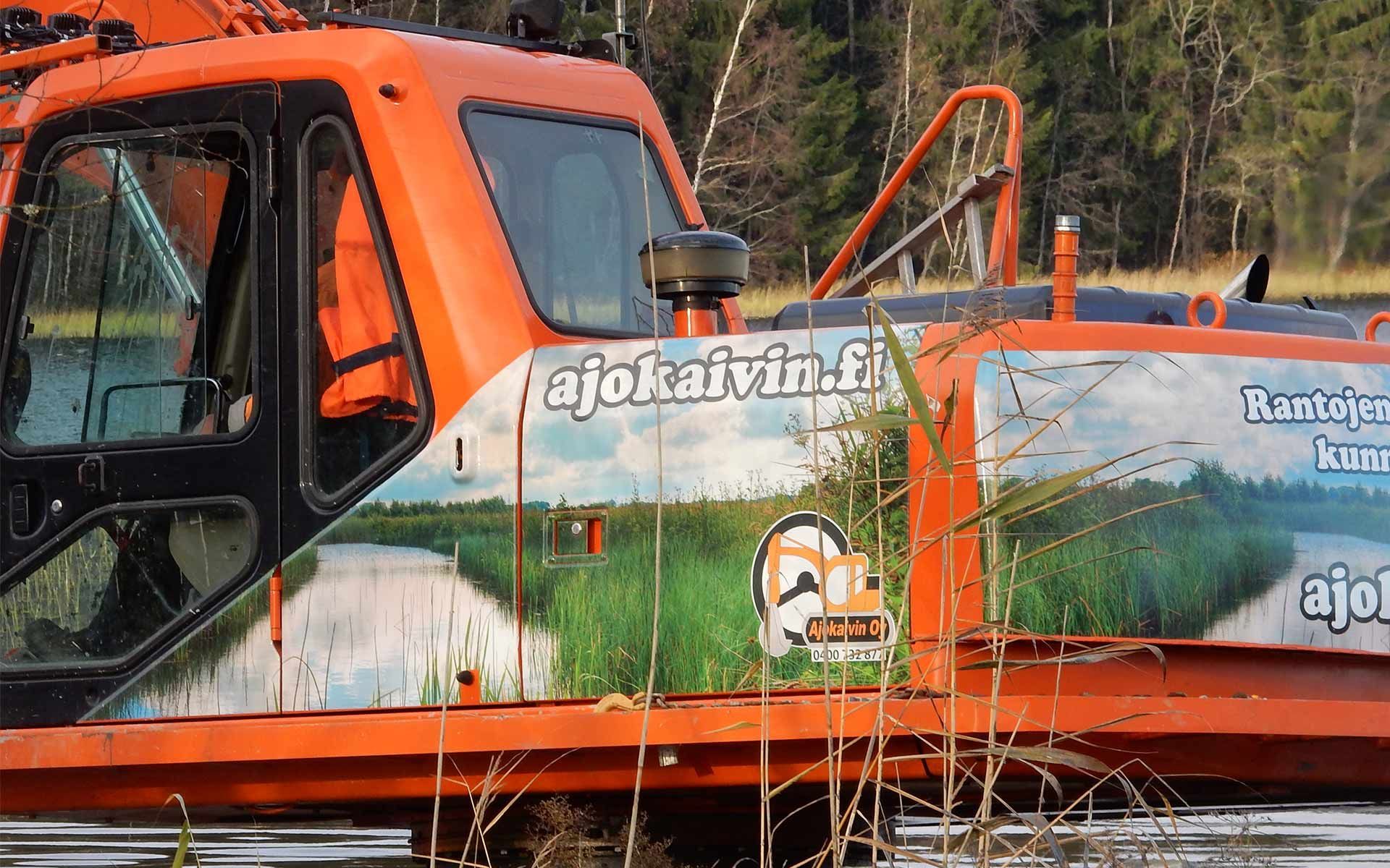 Oranssinvihreä kuorma-auto, jossa on sininen sivupaneeli ja oranssit varusteet metsäalueella.