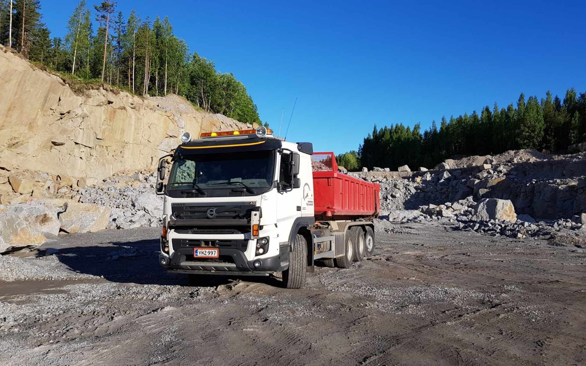 Valkoinen kippiauto punaisella lavalla soratietä pitkin kirkkaan sinisen taivaan alla