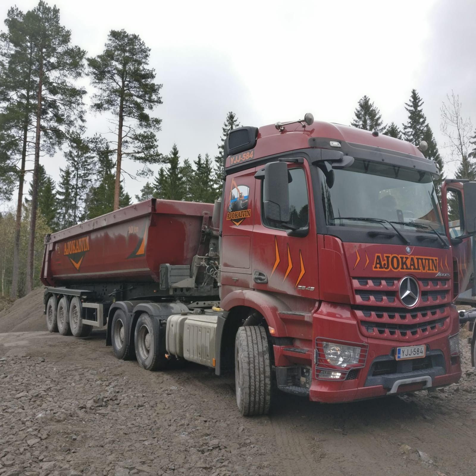 Punainen kuorma-auto mutaisella tiellä mäntymetsässä