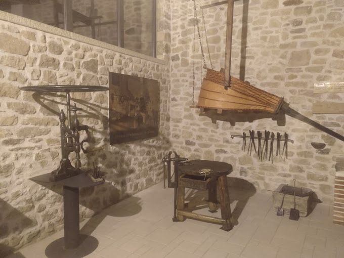 Una habitación con una pared de piedra, un taburete de madera, una mesa y un cuadro en la pared.