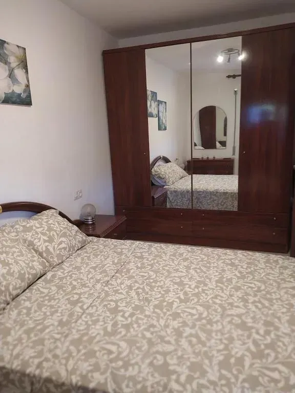Un dormitorio con cama, mesita de noche, armario y espejo.