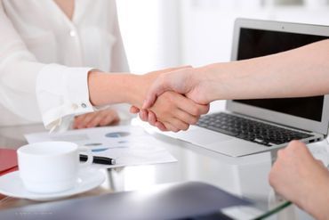 eine Person im Anzug steht vor einem Bücherregal mit verschränkten Armen