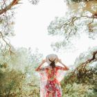 Una persona con un vestido y un sombrero estampados con flores está de pie bajo unos árboles.