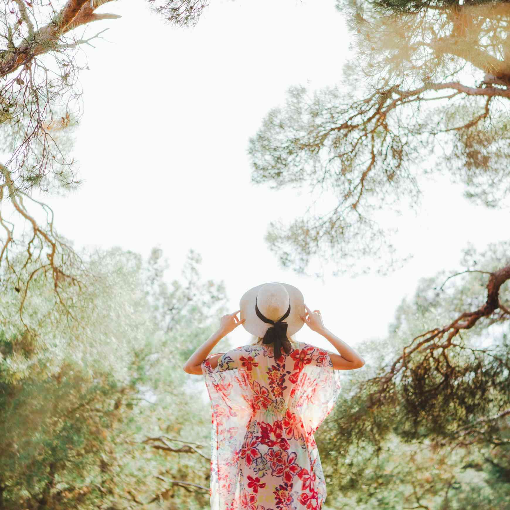 Una persona con un vestido y un sombrero estampados con flores está de pie entre los árboles.