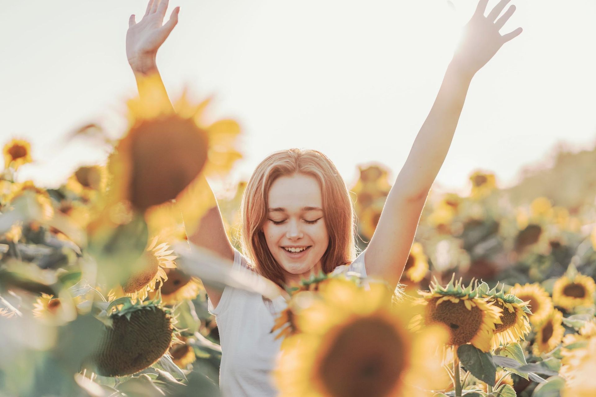 Una persona sonríe en un campo de girasoles con los brazos en alto bajo la cálida luz del sol.
