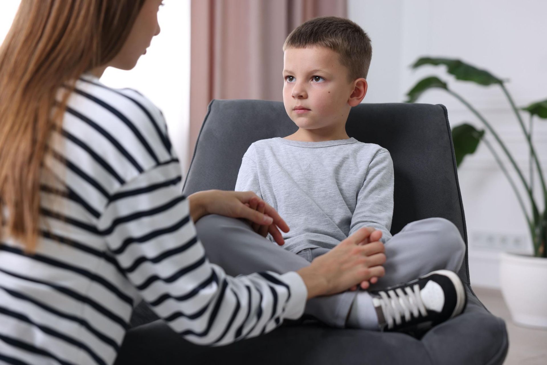 Terapeuta hablando con un niño sentado en una habitación 상담, ambos mirándose el uno al otro.
