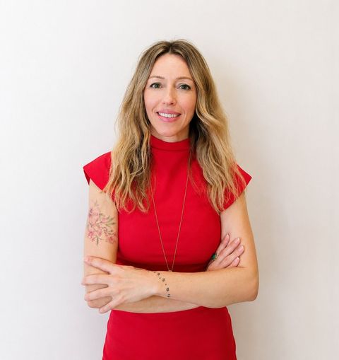 Mujer con vestido rojo de pie con los brazos cruzados sobre un fondo claro liso.
