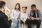 Un consejero se reúne con una familia en un sofá para hablar sobre un niño que sostiene una tarjeta con una carita sonriente.