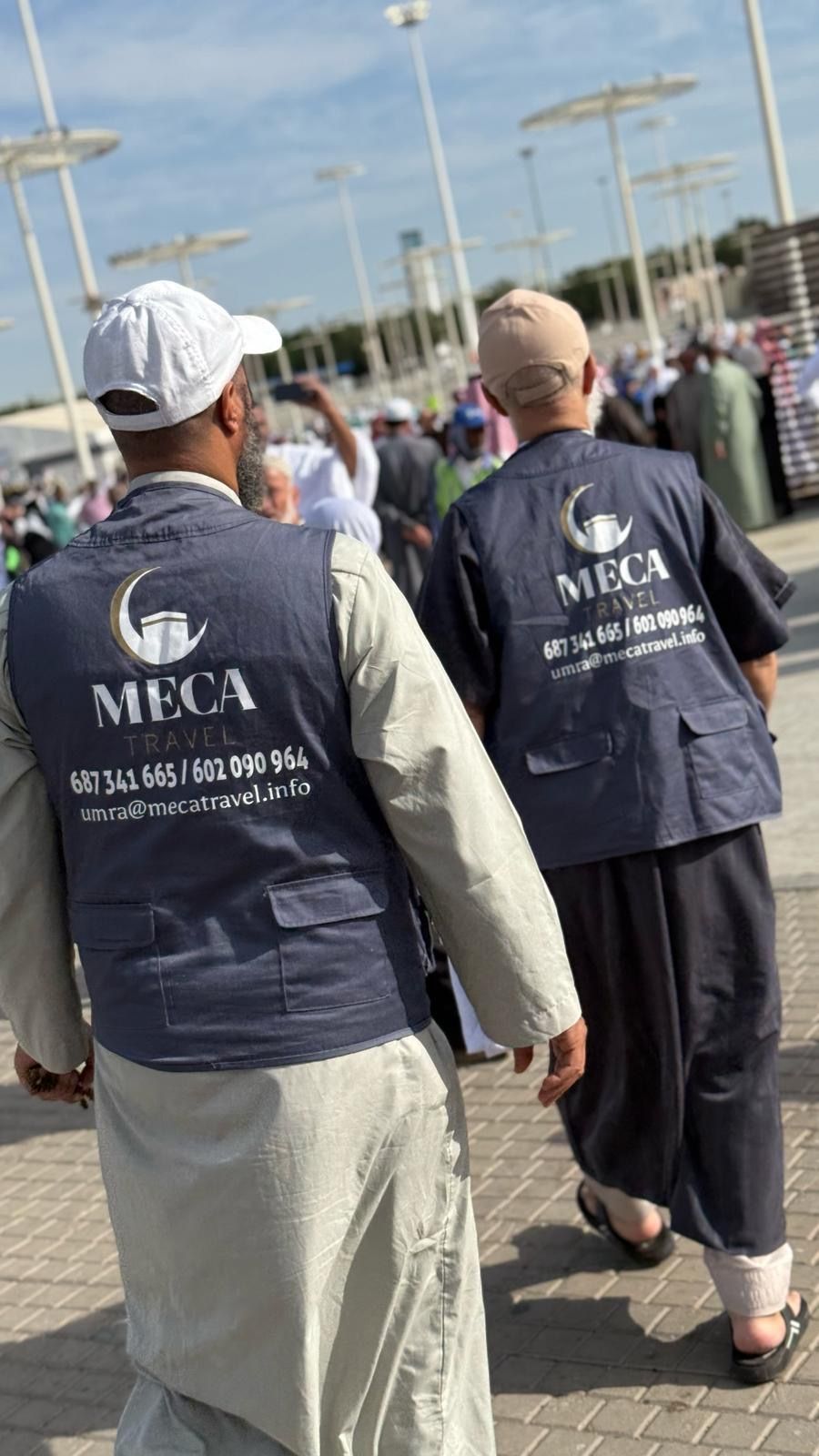 Dos personas con chalecos con el logotipo de MECA caminan en una zona exterior abarrotada.