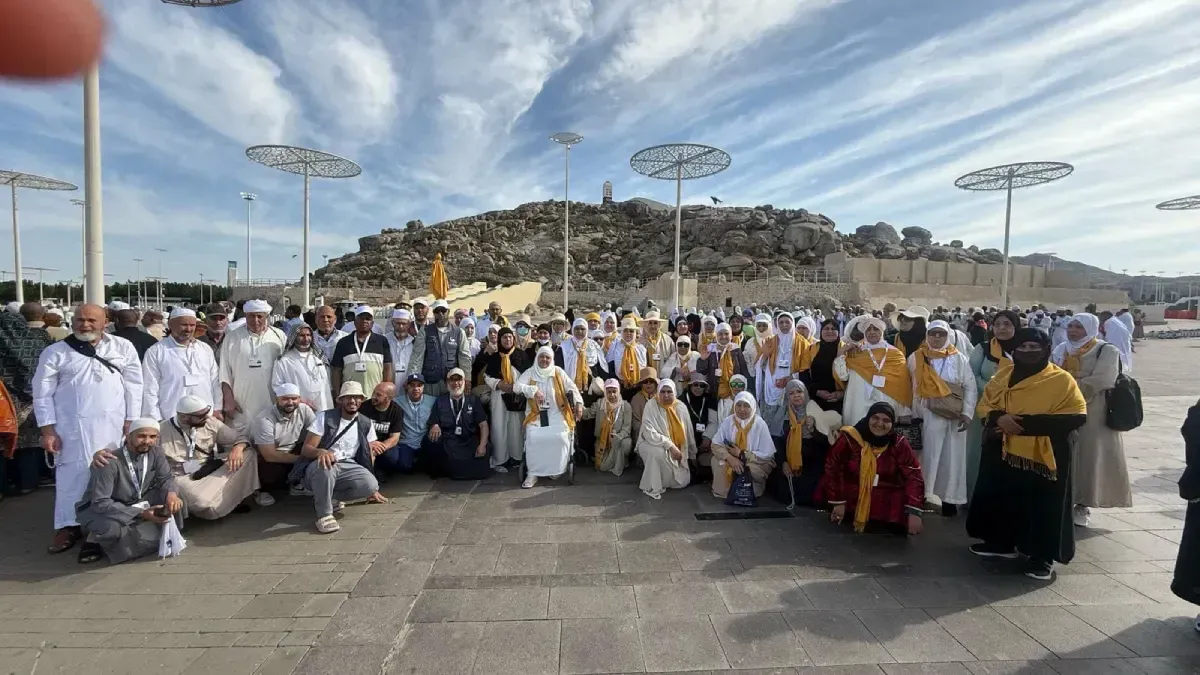 Un grupo de personas vestidas de blanco y amarillo posan al aire libre con una colina rocosa de fondo.