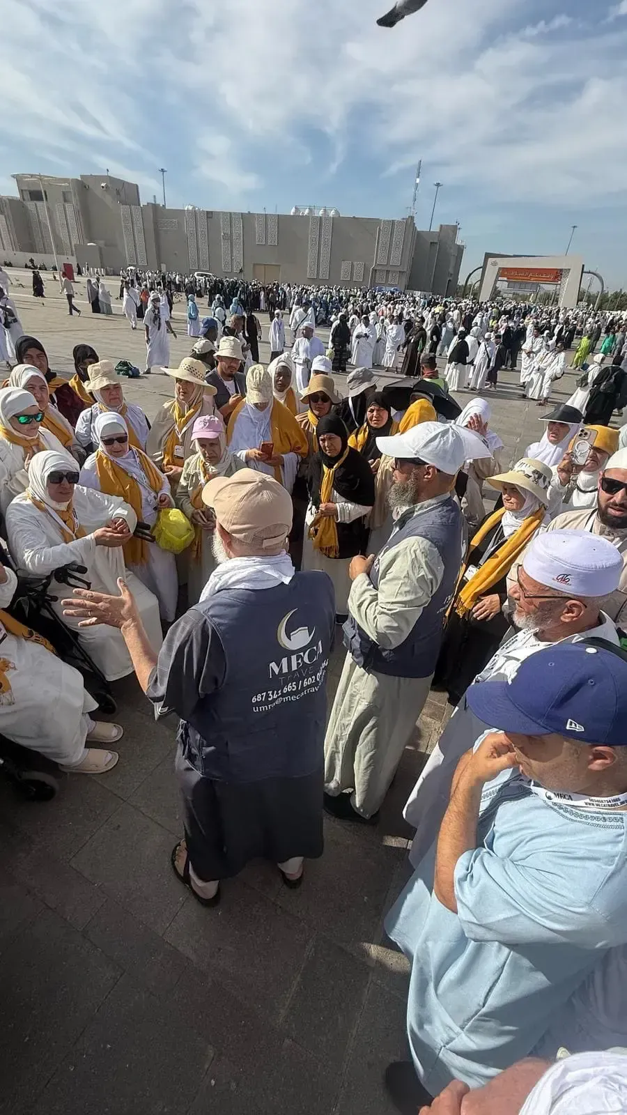 Un numeroso grupo de personas vestidas de blanco y con sombreros se reúne al aire libre en un espacio público.