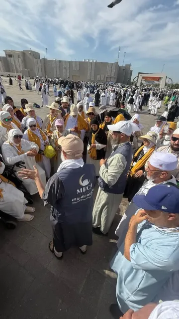 Un numeroso grupo de personas vestidas de blanco y con sombreros se reúne al aire libre en un espacio público.