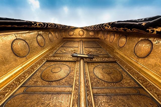 Puerta dorada de la Kaaba en La Meca, Arabia Saudita, con elaboradas tallas y un cielo nublado.