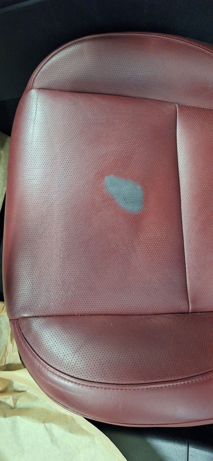 Gros plan sur un siège auto en cuir bordeaux avec une tache bleu foncé au centre. Le siège est perforé.